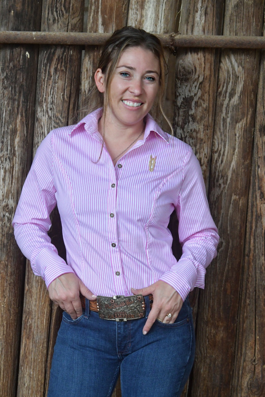 Woman wearing a pink pinstripe shirt and blue jeans standing against a wooden wall.