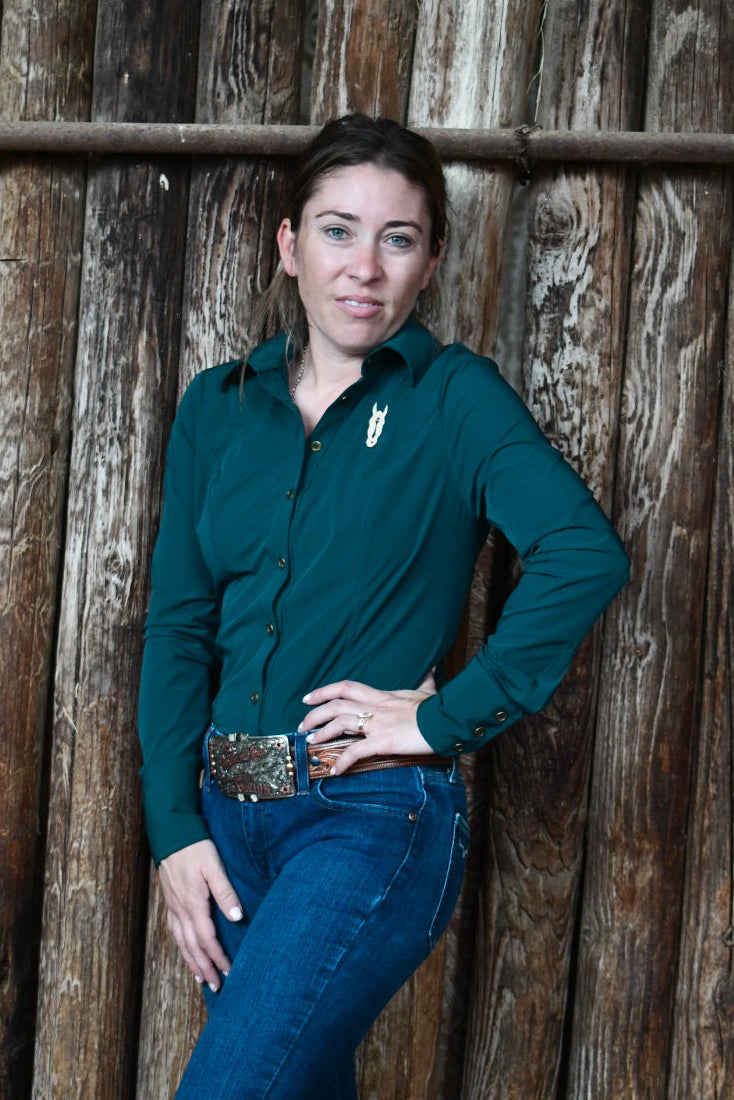 Woman in a teal green shirt and blue jeans standing against a wooden fence.