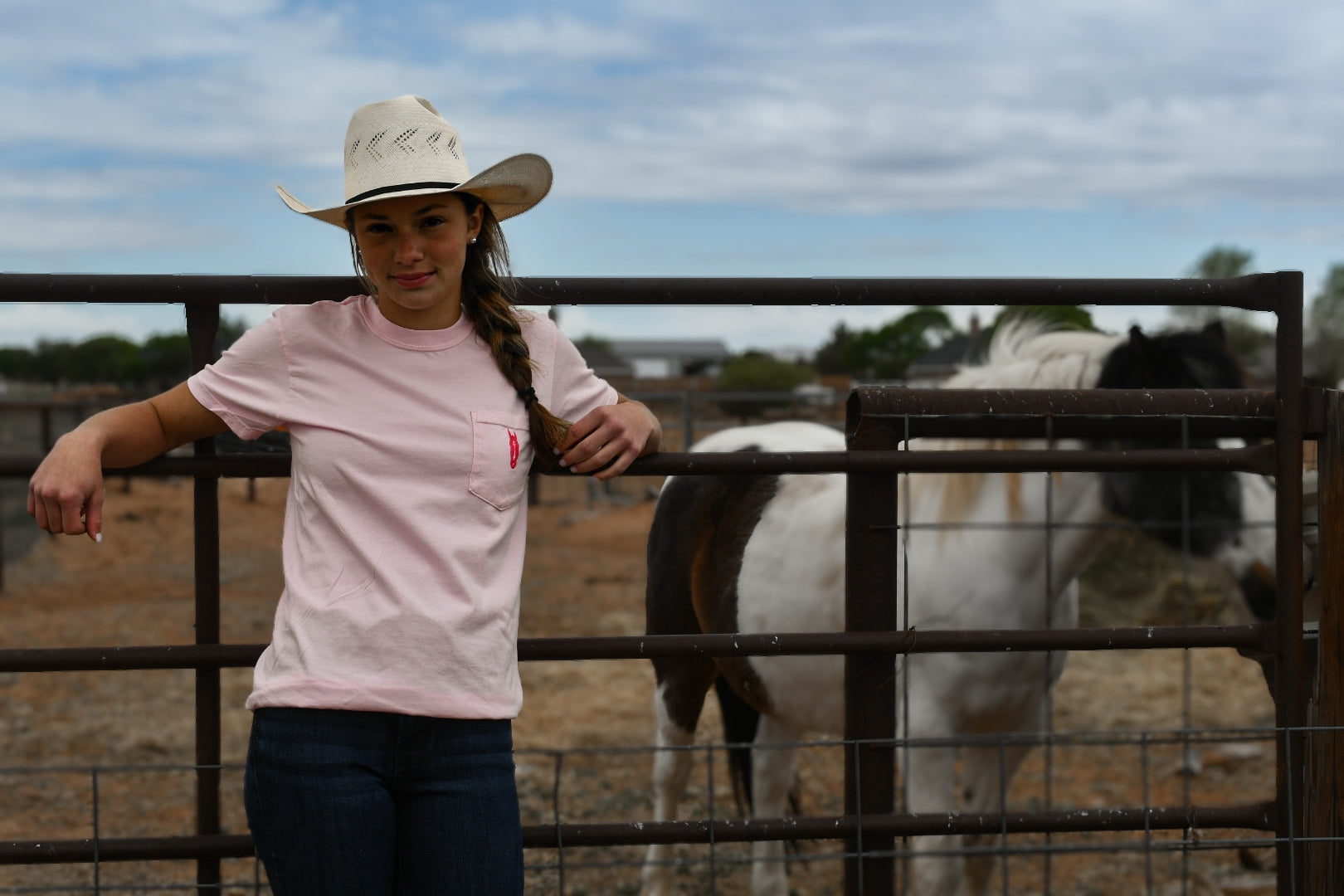 Person wearing a cowboy hat and pink shirt standing next to a horse in a fenced area.