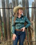 A woman wearing a dark green satin button-up shirt with a collared neckline, standing outdoors in front of a wooden fence.
