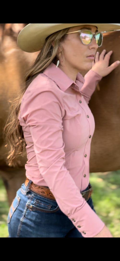 Woman in pink fitted and moisture wicking rodeo shirt and cowboy hat standing next to a horse