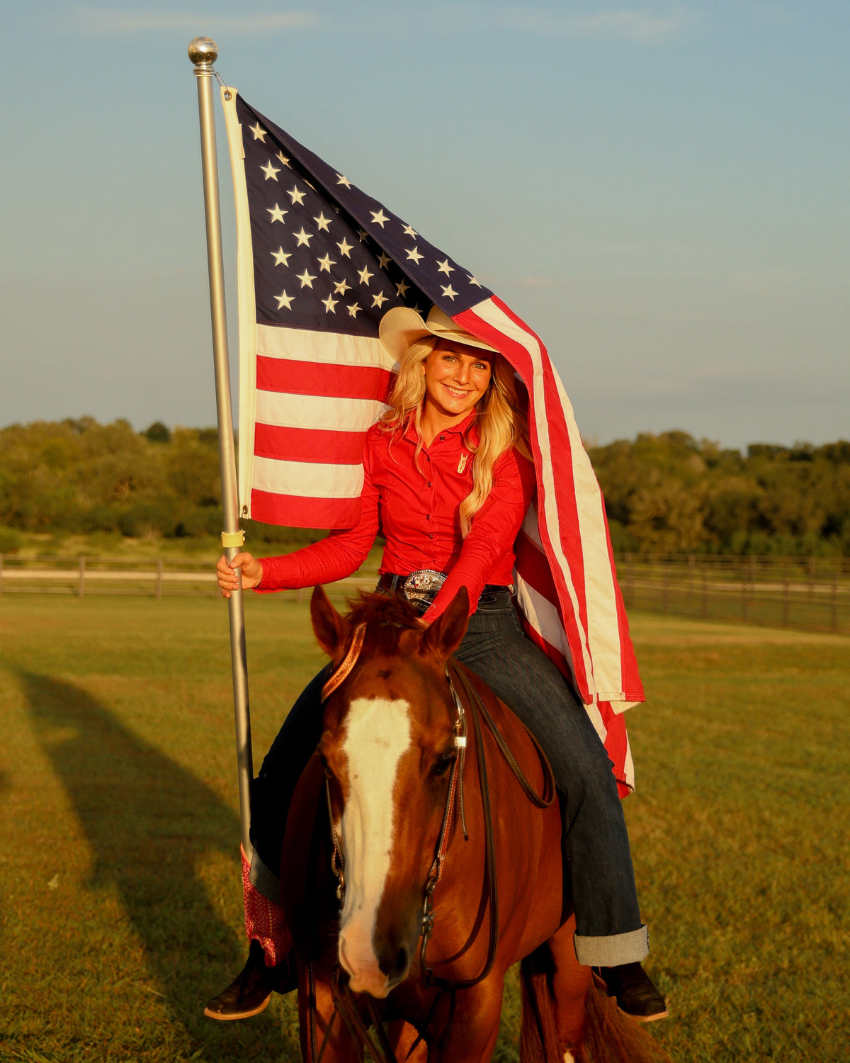 cowgirl horseback with an American flag wearing a fitted red rodeo shirt