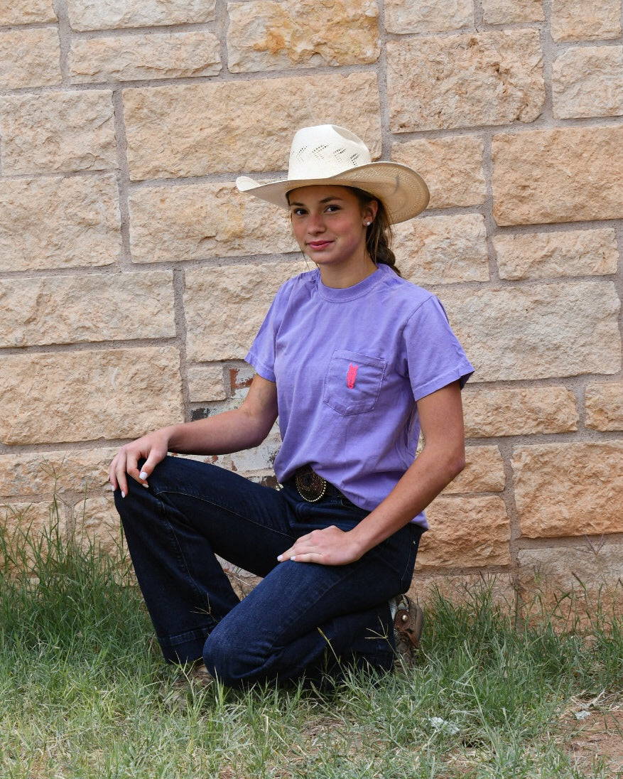 Person wearing a purple shirt and cowboy hat sitting against a stone wall.